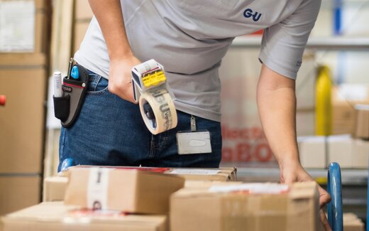 Mitarbeiter verpackt Kartons mit Klebeband im Lager