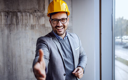 Mann in Anzug und Bauhelm mit Handschlag