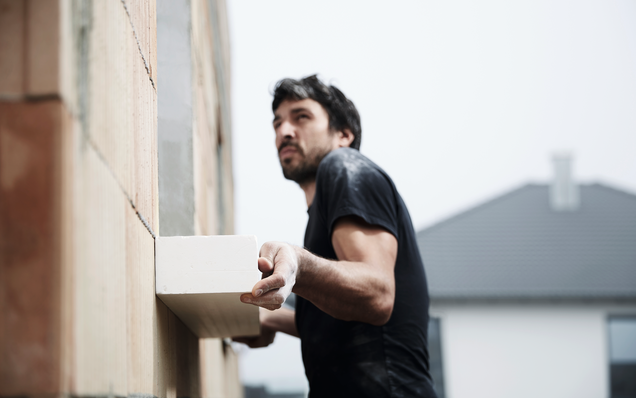 İnşaat işçisi, kaba inşaat sırasında GU ön montaj kasasını bir ev duvarına monte ediyor